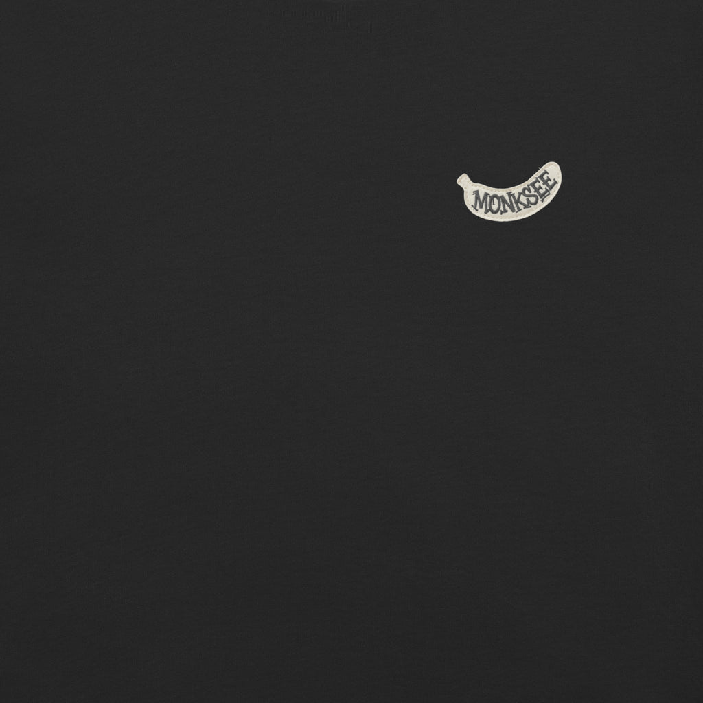 A white banana shaped Monksee label from the front left chest of a black t-shirt