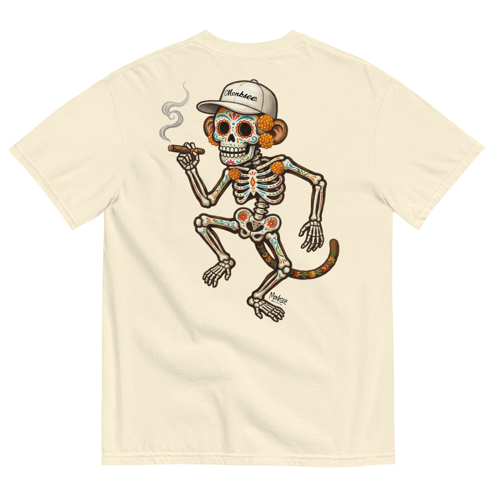A bone-colored short-sleeve t-shirt showing the back side, which features a large graphic of a Day of the Dead skeleton monkey wearing a white baseball cap and smoking a cigar.