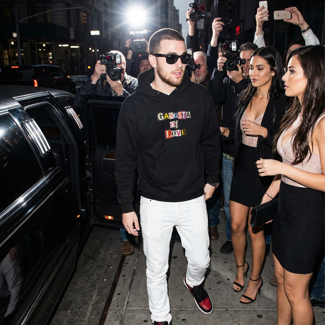 Celebrity in a black Monksee Gangsta of Love hoodie walking past a limousine with paparazzi taking photos.