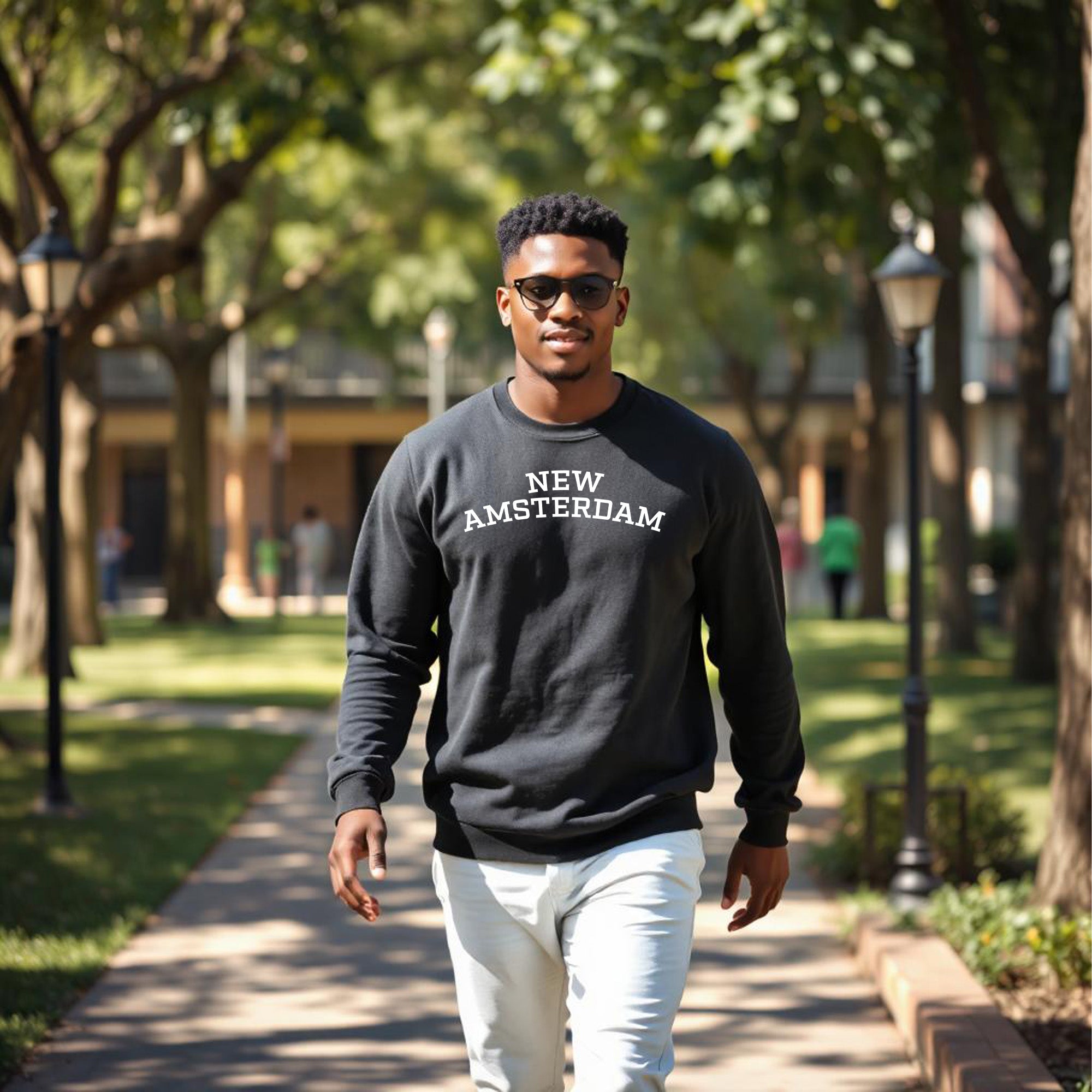 Man wearing a 'New Amsterdam' sweatshirt walking on a tree-lined path.