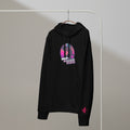 A black Monksee "Drop the Vibe" hoodie hanging on a rack against a white background. It features a neon graphic of a cap-wearing monkey against a sunset with palm trees, with "DROP the VIBE" in bold pink and white text. A small pink Monksee banana logo is on the left sleeve