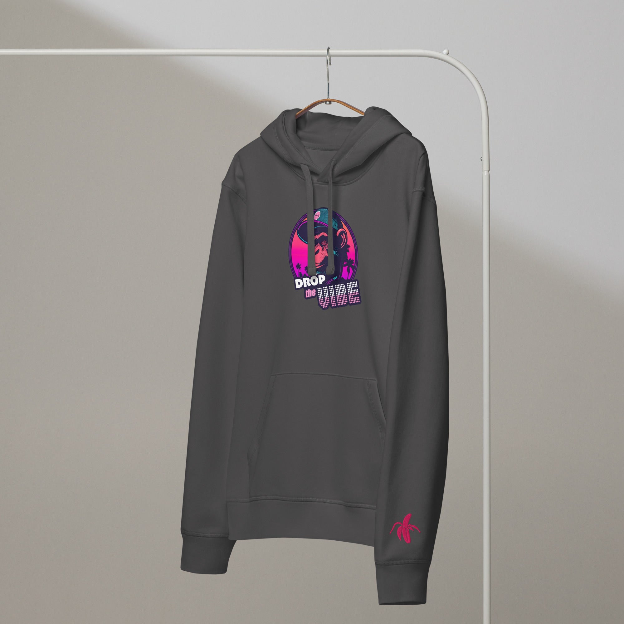 A anthracite Monksee "Drop the Vibe" hoodie hanging on a rack against a white background. It features a neon graphic of a cap-wearing monkey against a sunset with palm trees, with "DROP the VIBE" in bold pink and white text. A small pink Monksee banana logo is on the left sleeve