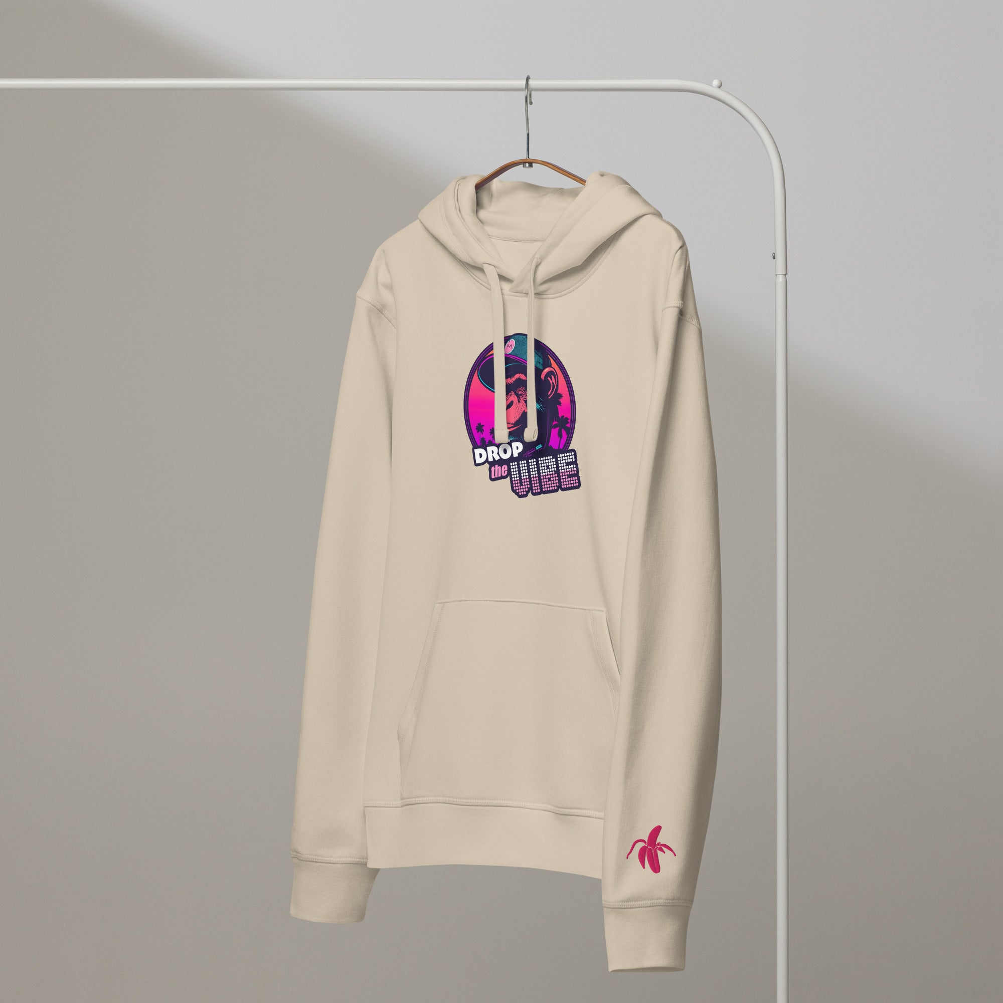 A desert Monksee "Drop the Vibe" hoodie hanging on a rack against a white background. It features a neon graphic of a cap-wearing monkey against a sunset with palm trees, with "DROP the VIBE" in bold pink and white text. A small pink Monksee banana logo is on the left sleeve