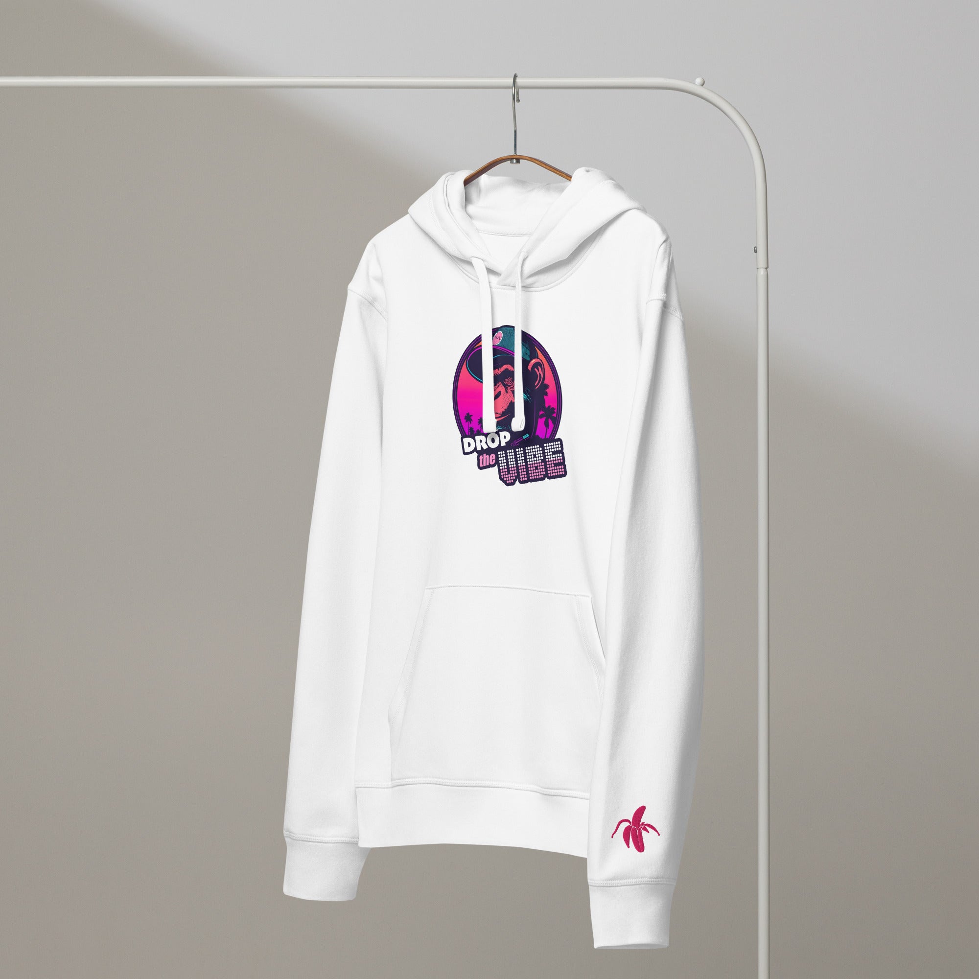 A white Monksee "Drop the Vibe" hoodie hanging on a rack against a white background. It features a neon graphic of a cap-wearing monkey against a sunset with palm trees, with "DROP the VIBE" in bold pink and white text. A small pink Monksee banana logo is on the left sleeve