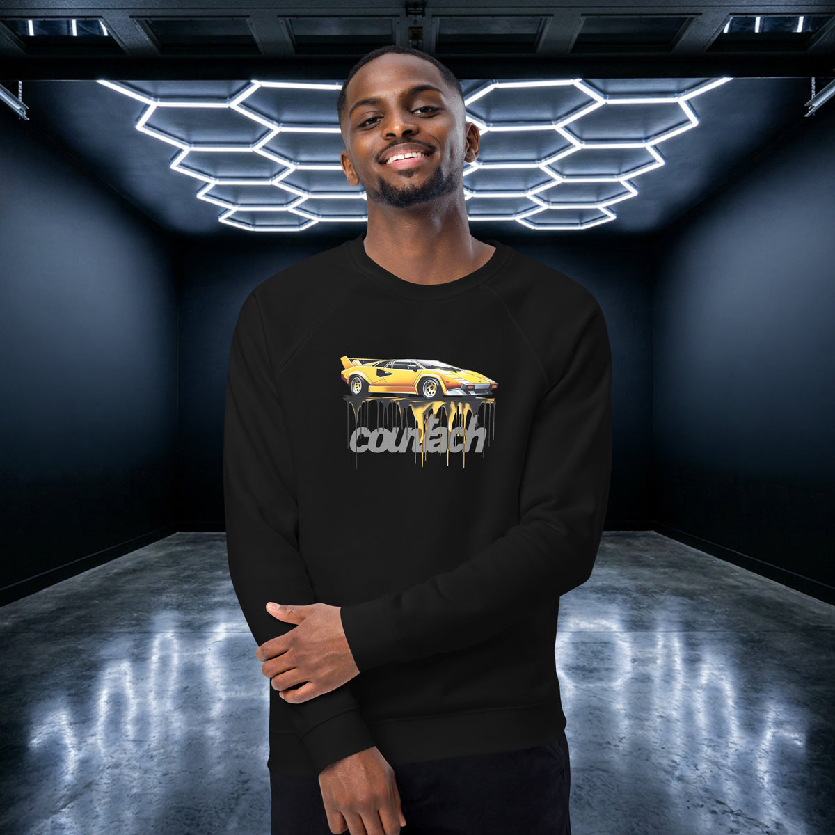 Monksee EPIC Countach organic raglan sweatshirt in black, worn front-on in a honeycomb-lit garage, showing the yellow Lamborghini Countach graphic