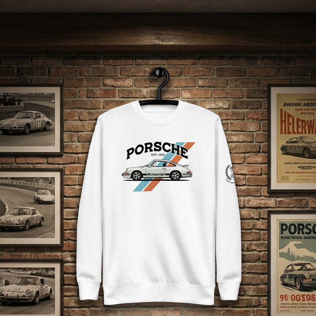 A white crewneck sweatshirt hanging on a black hanger against a brick wall backdrop. The sweatshirt features a graphic print of a classic Porsche 911 car with the text 'PORSCHE' and '911' above it, accented by blue and orange diagonal stripes.